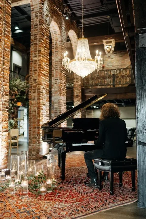 piano player with a chandelier hanging and the walls and columns covered in old bricks