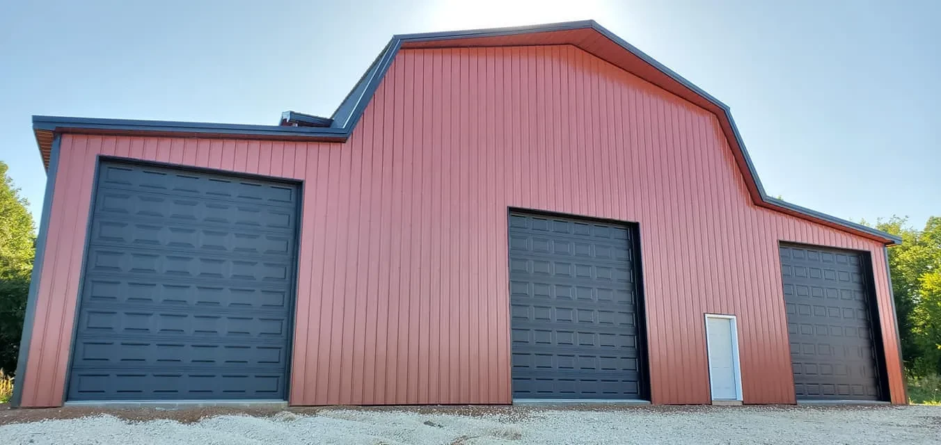 Red steel barn with black oversized garage doors built by Stellan Eoin Builders, featuring durable metal siding and a modern gambrel roof design.