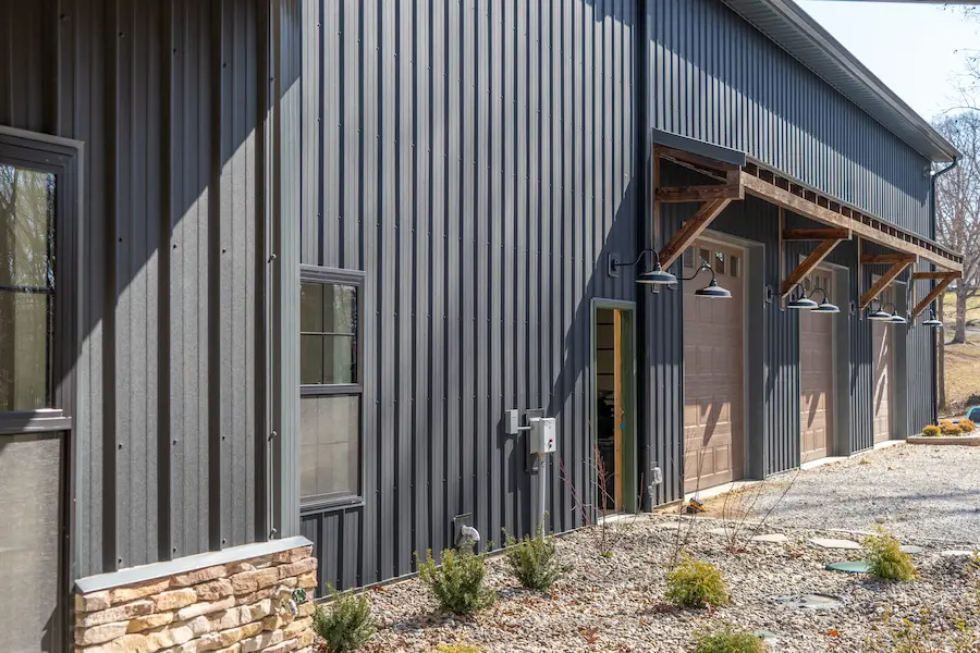 Black metal workshop with wood awnings, barn lighting, and stone accents built by Stellan Eoin Builders.