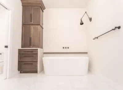 white modern bathtub with brown linen cabinet next to it