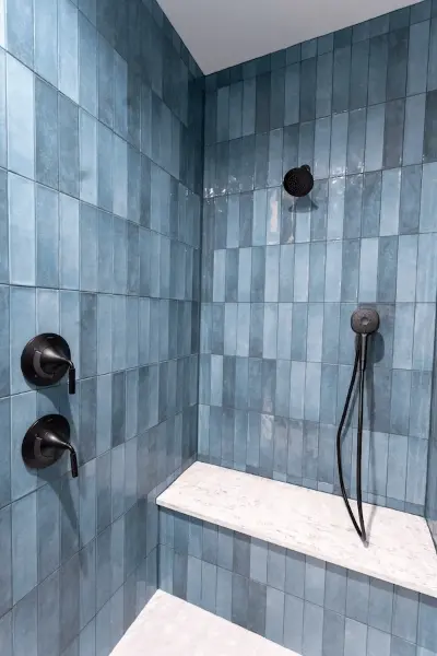 Multi colored blue tiled walk-in master shower with a white tiled bench